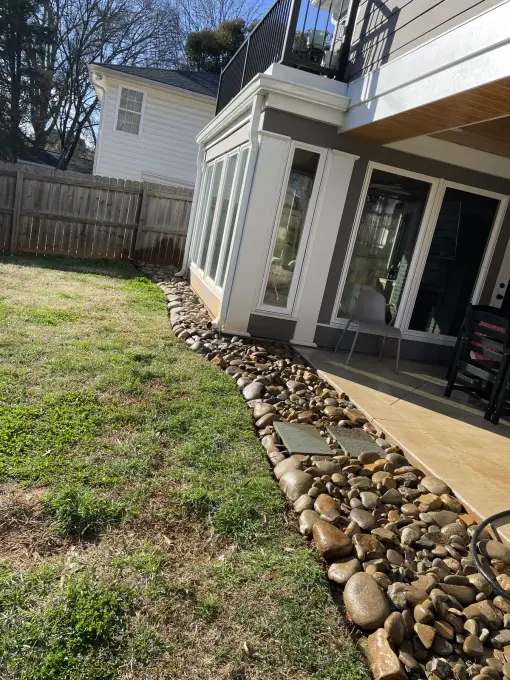 River-rock drainage bed running alongside a paver walkway at the base of a screened porch