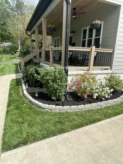 Curved planting bed edged with pavers and filled with flowering shrubs along a front porch and lush lawn