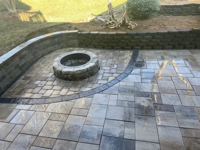 Paver patio featuring a round stone fire pit and a curved paver seating wall