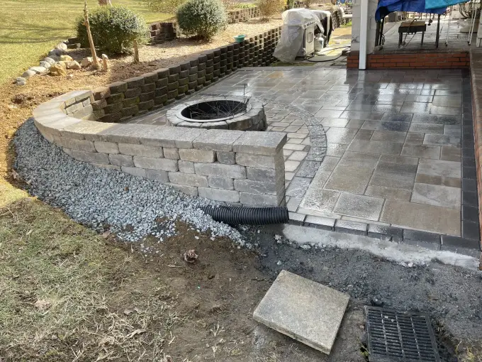 Raised paver patio with a fire pit and retaining wall built into a sloped yard
