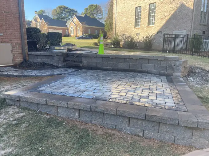 Raised paver patio bordered by a retaining wall behind a brick home