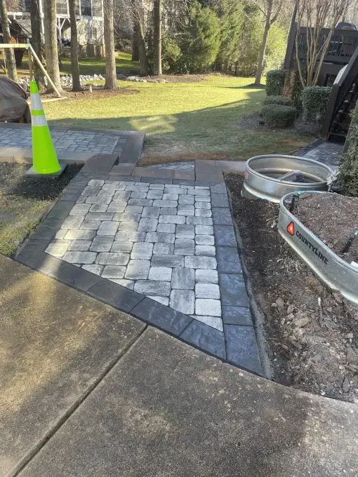 Paver patio and walkway with a steel fire pit ring set in a landscaped backyard