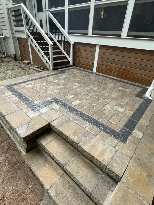 Tan paver patio with a contrasting charcoal border and steps leading up to a screened porch