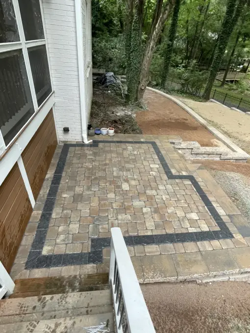 Paver patio with a dark banded border installed beneath a screened porch in a wooded yard