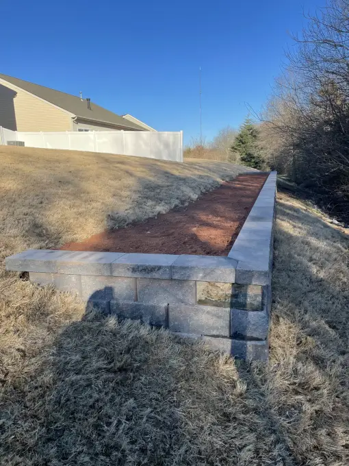 Stacked-block retaining wall with a stepped corner holding back a graded slope