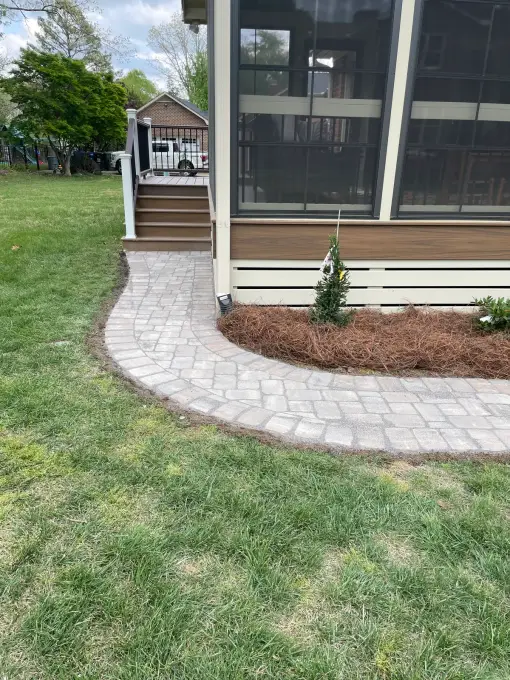 Curved paver walkway leading to a screened porch, edged with a fresh mulch bed and green lawn