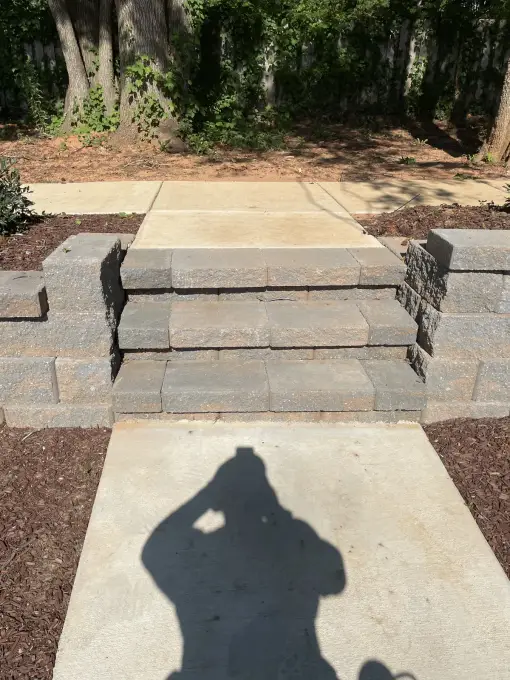 Stacked paver-block steps leading down to a concrete walkway between garden beds