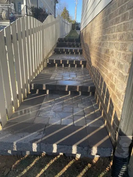 Paver walkway with steps running through a narrow side yard between a house and privacy fence