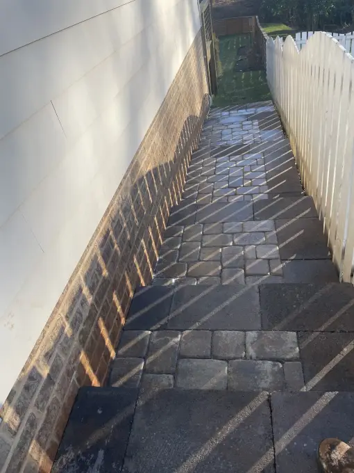 Cobblestone paver walkway threading a tight side yard beside a white privacy fence
